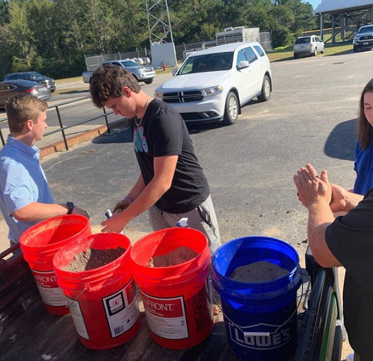 Students grab a handful of soil from one of four buckets and add water to determine the texture of the soil sample