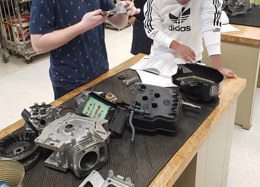 Students inspect small engine parts on a shop table as they prepare to reassemble the small engine.